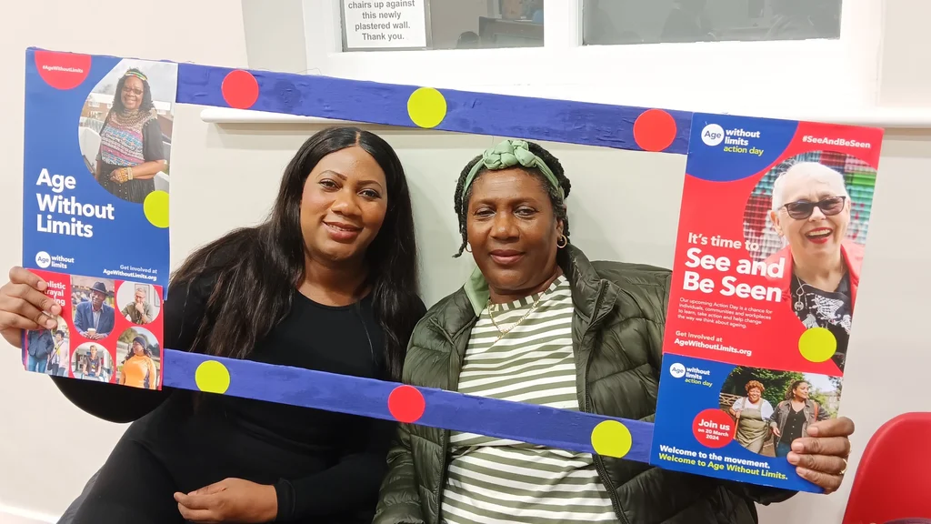 Two women pose next to an Age Without Limits banner