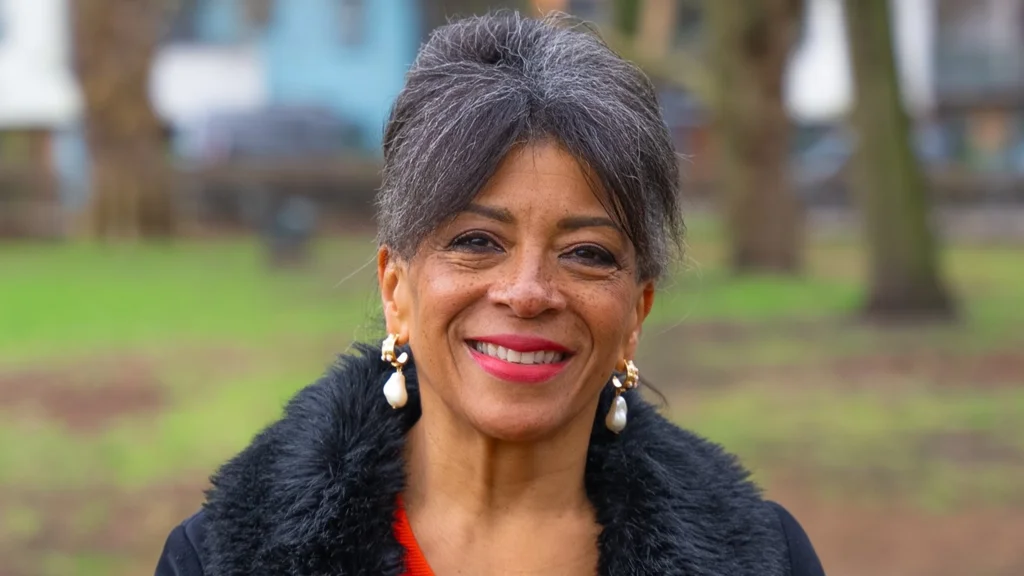 Colleen smiles at the camera with grass and trees behind her