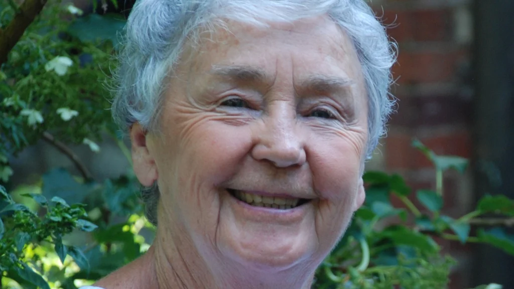 Dolores smiles at the camera with green tree leaves behind her