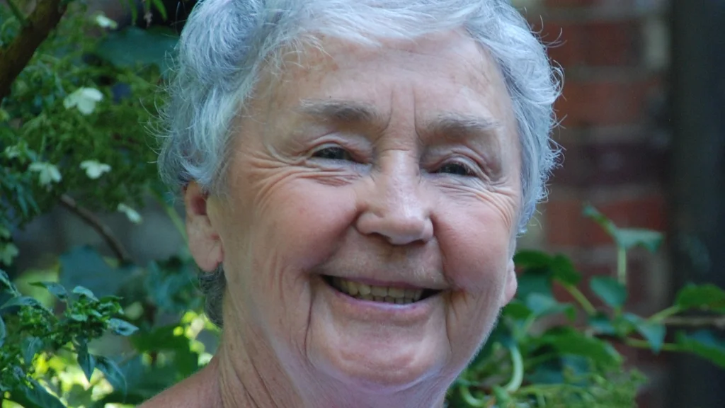 Dolores smiles at the camera with green tree leaves behind her