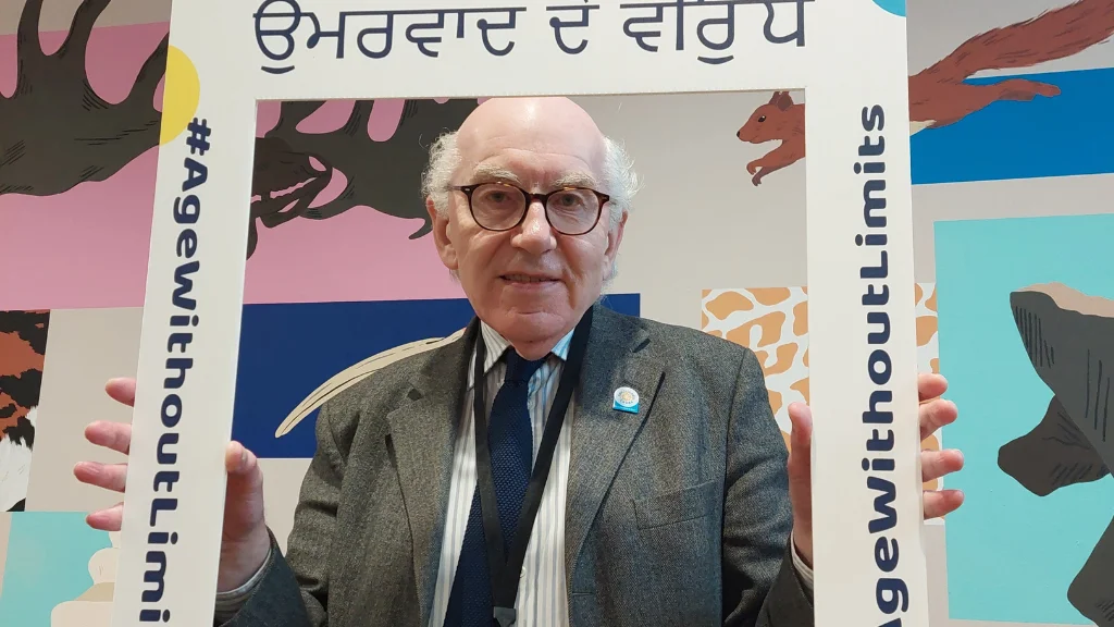 An older man holds a selfie frame with Against Ageism, Age Proud written in Punjabi.