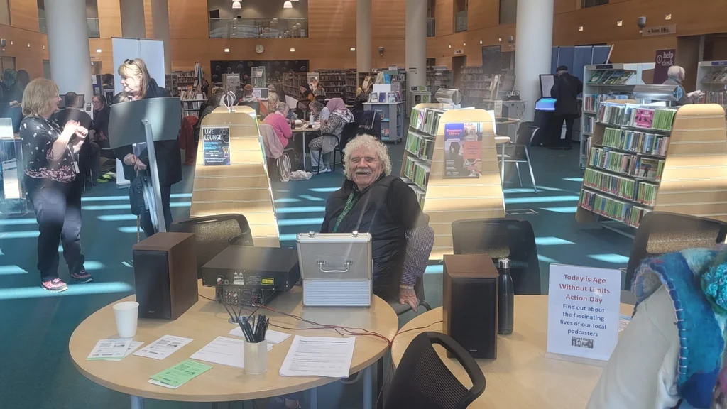 DJ King Jerry sits behind DJ decks on a desk in a library