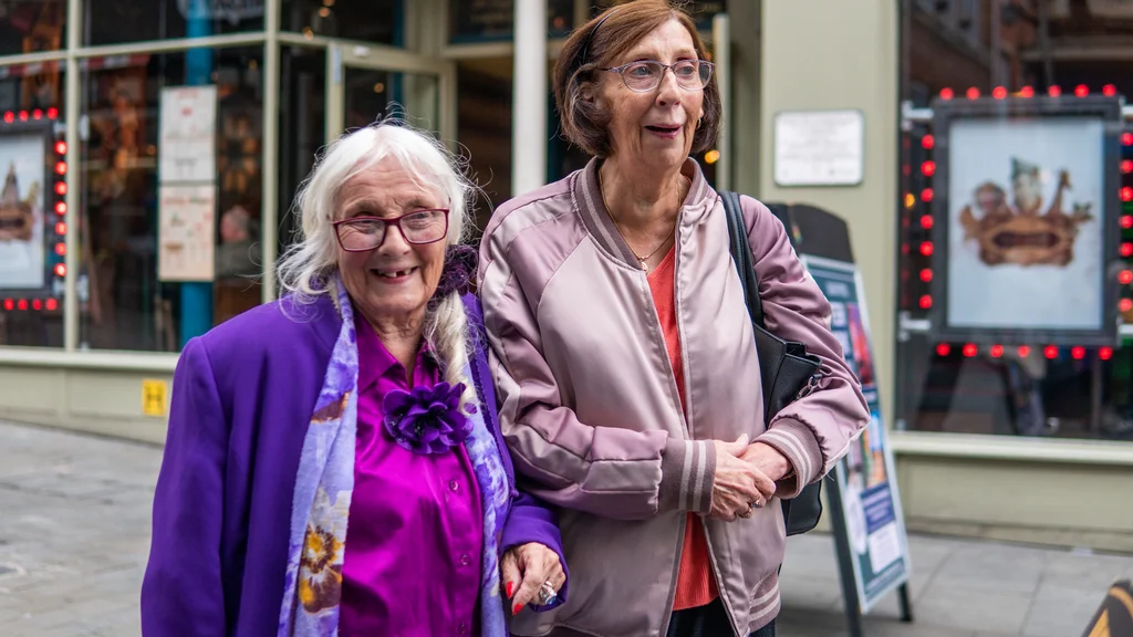 Two older women standing in a street with a restaurant in the background